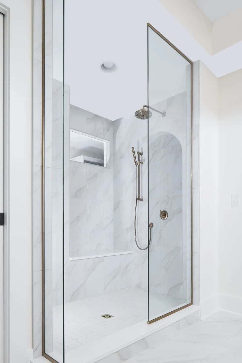 Marble-lined shower with a frameless glass door in a remodeled bathroom