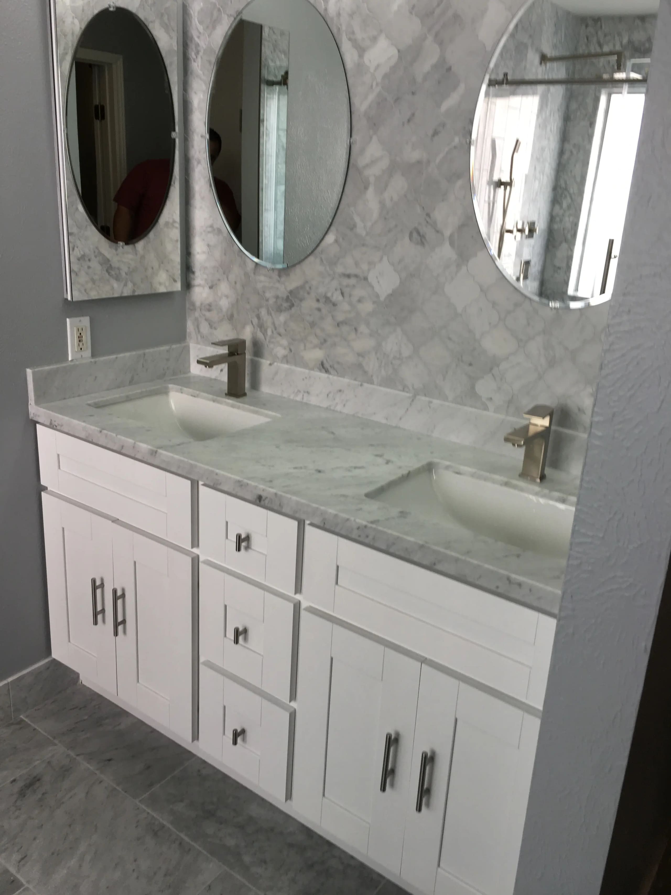 White double vanity with marble counter, marble-tiled wall and three oval mirrors