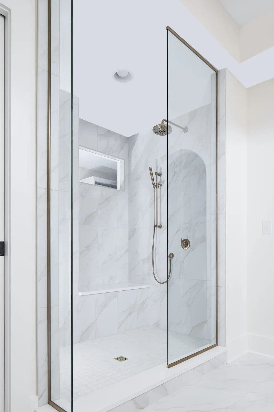 Marble-lined shower with a frameless glass door in a remodeled bathroom