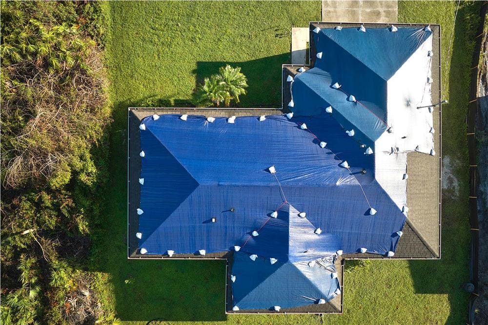 Aerial view of a blue tarp secured across a damaged roof